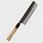 A 67-layer Damascus steel kitchen knife with a hammered blade and an olive wood handle, shown diagonally on a dark blue background with text overlays and red bell pepper props.