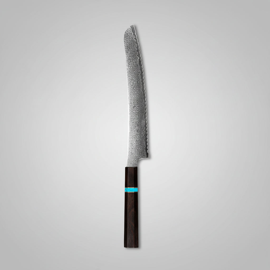A serrated bread knife with a dark wooden handle and a textured silver blade, placed diagonally on a round wooden cutting board. The board is styled with sliced artisanal bread, small dollops of white cream with strawberries, a bowl of fresh strawberries and blueberries, and a small dish of red sauce on a dark gray surface.