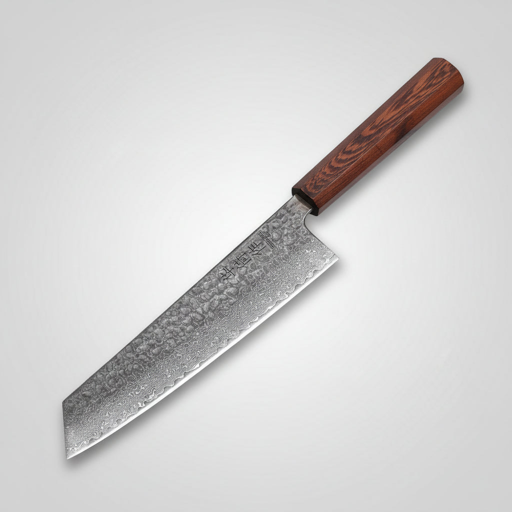 A kitchen knife with a dark wood handle and patterned steel blade rests diagonally on a wooden cutting board with raw beef, rosemary, garlic, and a bowl of cooked potatoes on a dark stone surface.