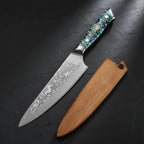 A Damascus steel chef's knife with a patterned blue and green handle, shown next to its wooden sheath on a plain white background.
