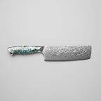 A Nakiri knife with a patterned Damascus steel blade and an iridescent abalone shell handle, displayed diagonally on a wooden cutting board with sliced cucumbers, kale, and a small bowl of radishes.