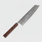 A Japanese-style kitchen knife with a hammered Damascus steel blade and a dark wood handle, placed diagonally on a wooden cutting board next to a raw beef steak garnished with cilantro.