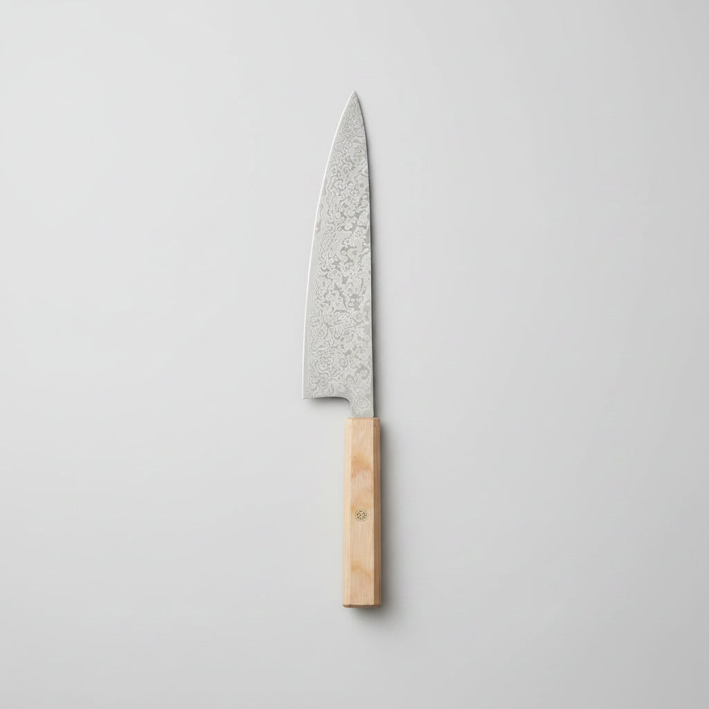 A kitchen knife with a patterned steel blade and a light wood handle resting on a wooden cutting board, surrounded by fresh rosemary, thyme, garlic, lemon slices, and a beige cloth on a marble surface.
