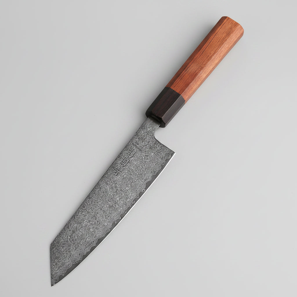 Steak on parchment paper with a knife on a wooden cutting board, surrounded by ingredients.