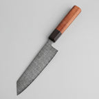 Steak on parchment paper with a knife on a wooden cutting board, surrounded by ingredients.