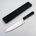 A professional chef's knife with a polished silver stainless steel blade and a black handle accented by a thin gold band, shown next to its sleek black presentation box on a white background.