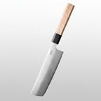 A 3-layer composite steel nakiri knife with a light wood handle and black collar, shown leaning on a wooden cutting board with sliced tomatoes and celery in a blurred kitchen setting. Text on the image reads '3 LAYER Composite Steel' and 'Nakiri Knife-6,5"'.