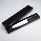 A black presentation box with its lid open, displaying a knife with a silver blade and a brown handle with red and gold accents, set against a plain white background.