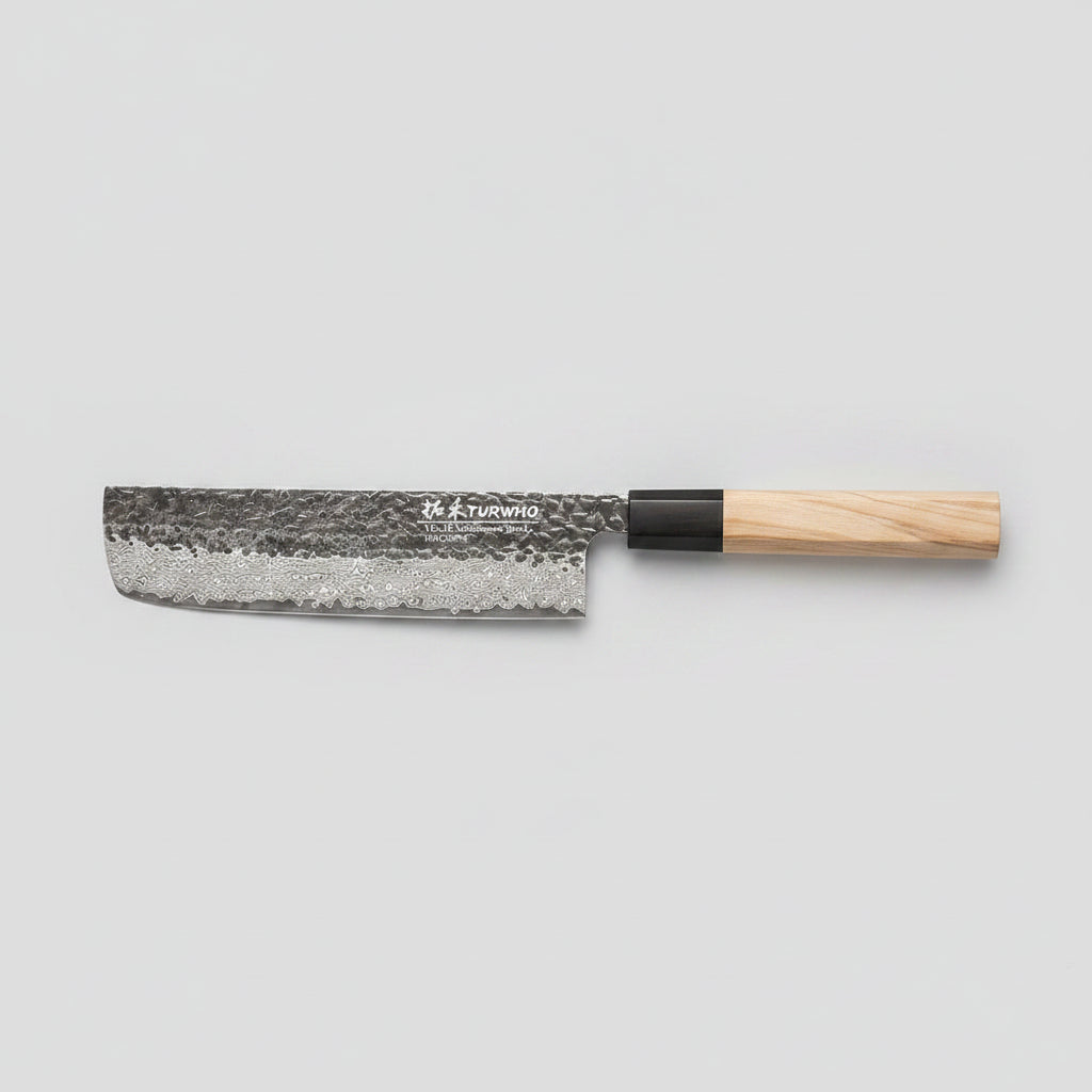 A Japanese-style kitchen knife with a hammered steel blade and a light wood handle, placed diagonally on a dark wooden cutting board surrounded by sliced red onion, whole onion, mushrooms, and cilantro.