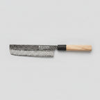 A Japanese-style kitchen knife with a hammered steel blade and a light wood handle, placed diagonally on a dark wooden cutting board surrounded by sliced red onion, whole onion, mushrooms, and cilantro.